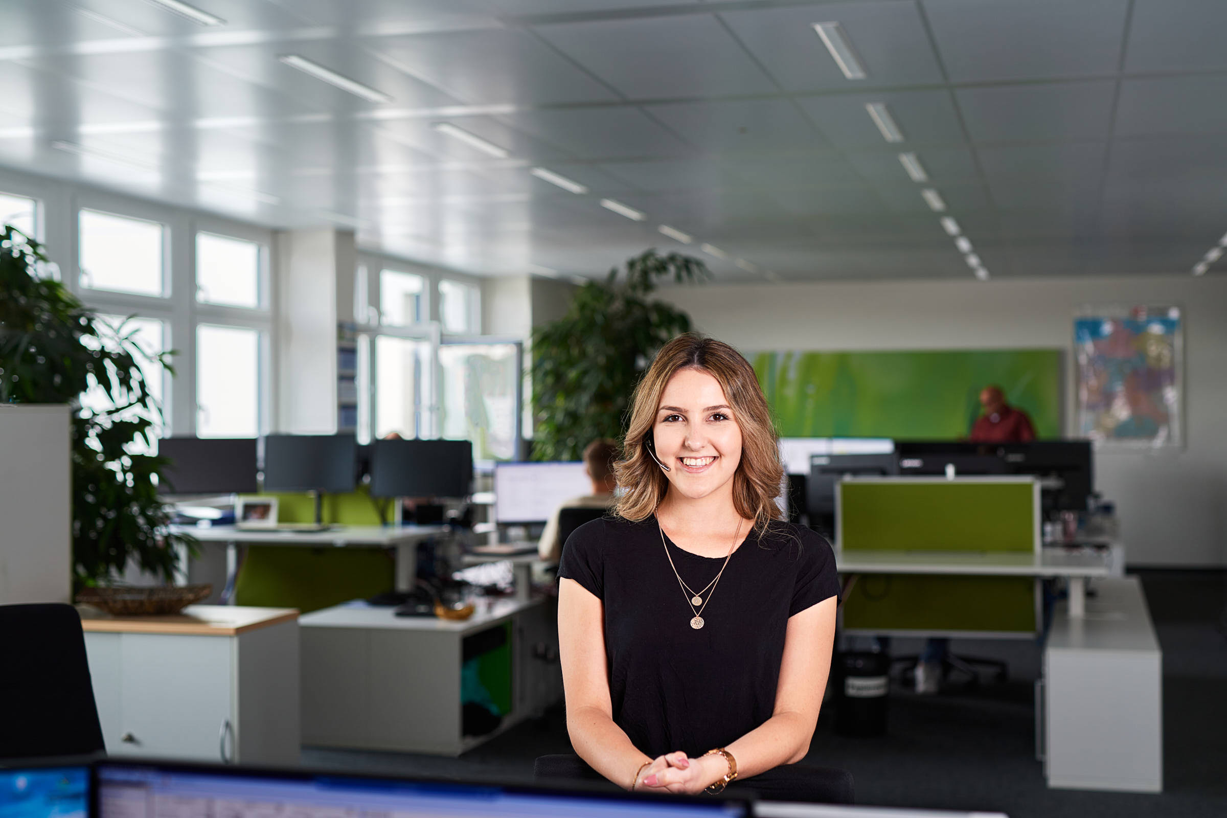 business-portrait-von junger-disponentin-die-im-grossraum-buero-steht